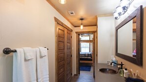 Un baño con puerta de madera, lavabo con artículos de aseo y espejo.