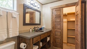 Un baño con tocador de madera, espejo, lavamanos y perchero para toallas.