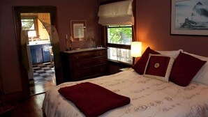 Um quarto com cama, cômoda, janela com vista e porta que dá para uma cozinha.
