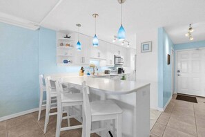 Una cucina con mobili bianchi, un'isola centrale bianca con sgabelli da bar, luci a sospensione e un forno a microonde.
