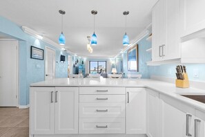 A modern kitchen with white cabinetry, a central island, pendant lighting, and a view to the outside.