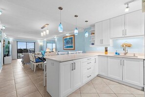 A modern kitchen with white cabinetry, pendant lighting, and a dining area with chairs and a table.