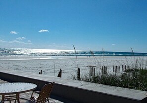 Blick auf einen Strand mit Tisch und Stühlen, einer Betonmauer und einem Holzzaun.