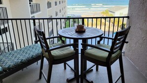 Ein Balkon mit Tisch und Stühlen mit Blick auf einen Strand und das Meer.