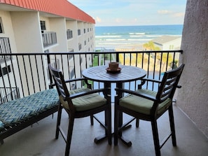 Ein Balkon mit Tisch und Stühlen mit Blick auf einen Strand und das Meer.