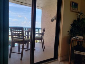 Enjoy the ocean view from this room's sliding glass door, featuring a comfortable chair, a small table, and a potted plant.