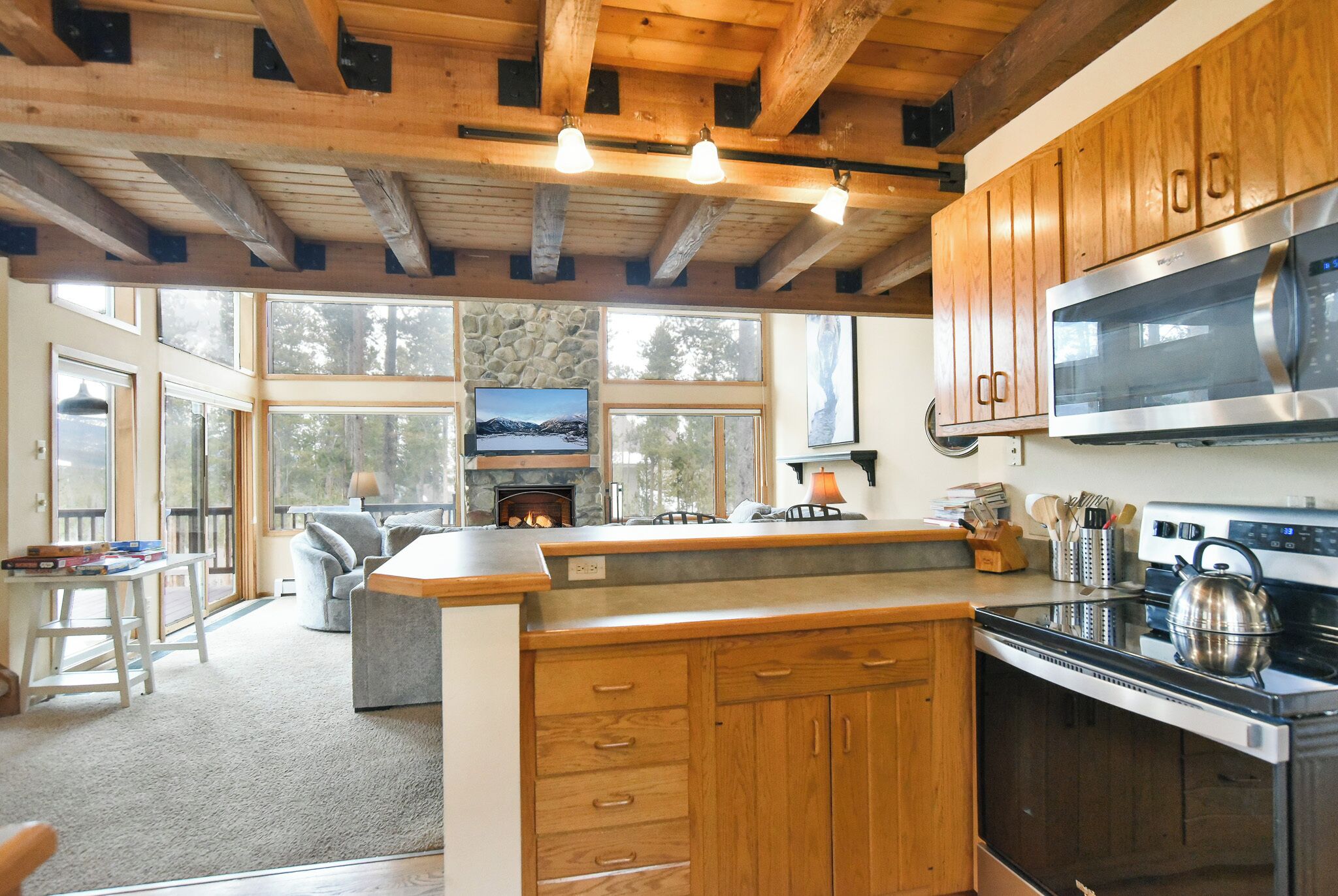 A spacious kitchen with wooden cabinets, a microwave, and a stove. There is a fireplace and a large window overlooking a scenic view.