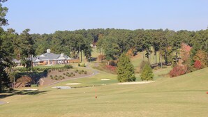 Un campo de golf con club house, árboles y un paisaje ondulado.