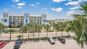 A multi-story hotel with a parking lot, palm trees, and a clear blue sky.