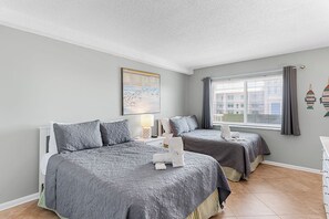 A hotel room with two beds, a large window with curtains, a painting on the wall, and a view of buildings outside. - Sand Castle I 401 - GULF FRONT WRAP BALCONY Condo! (Indian Shores)