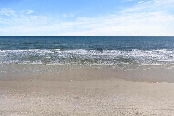 A beach with waves approaching the shore under a clear sky.