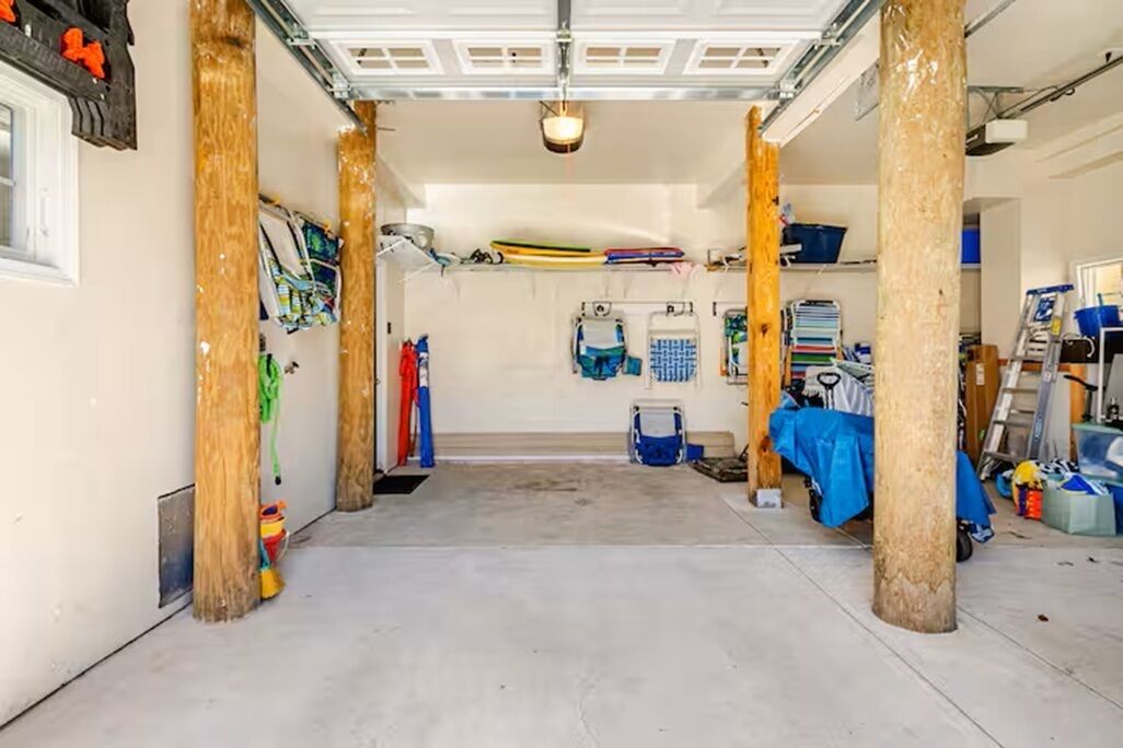 A garage with wooden pillars, a concrete floor, and various items like a kayak, a blue tarp, and a ladder.