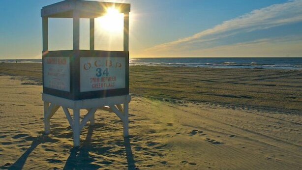 Una torre de salvavidas con la etiqueta "OCB 34" en una playa, con el sol brillando a trav és de su ventana.