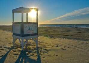 Une tour de surveillance, portant l’inscription « OCB 34 », se dresse sur une plage, le soleil brillant à travers sa fenêtre.