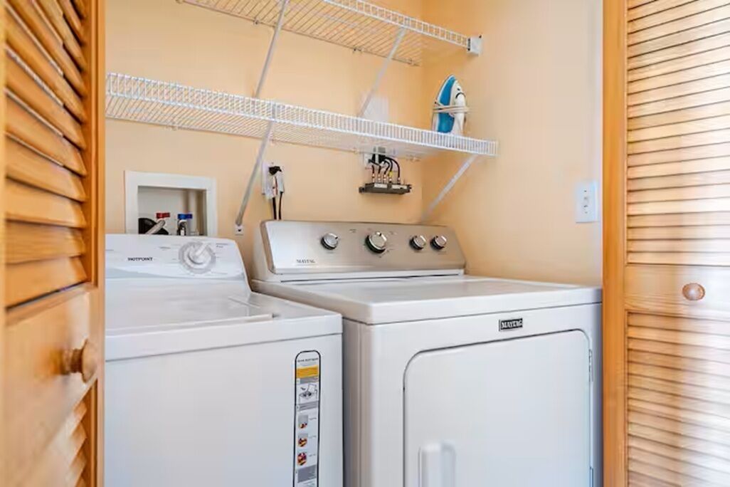 A laundry area with a washing machine, dryer, and a shelf with a blue container.