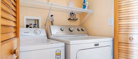 A laundry area with a washing machine, dryer, and a shelf with a blue container.