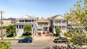 Una hilera de casas de dos pisos con porches delanteros, una escalera central y una entrada con coches estacionados.