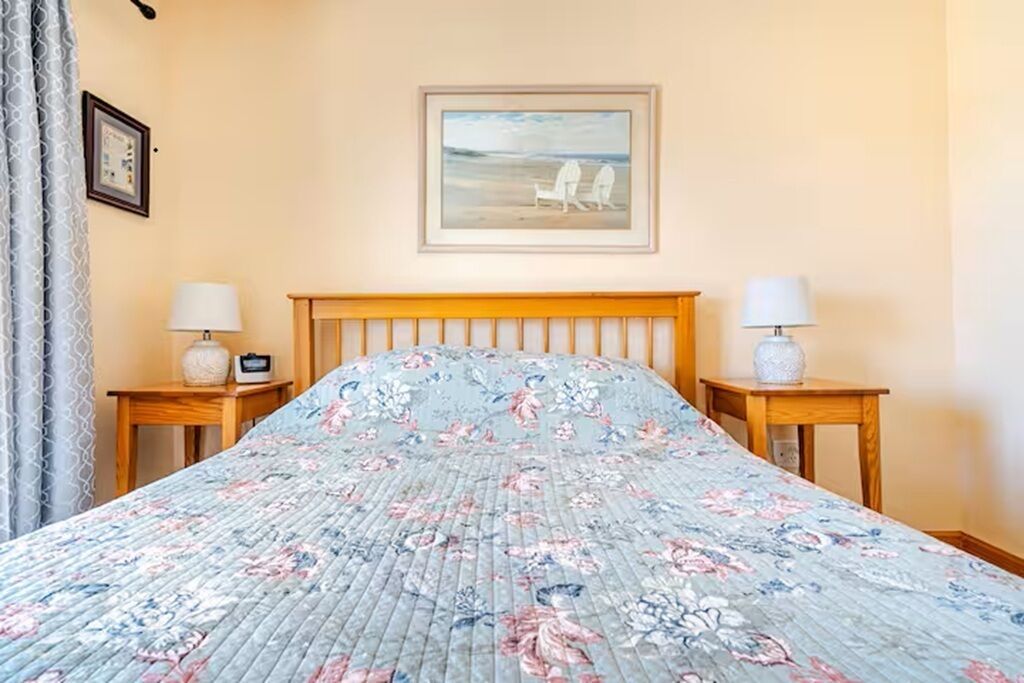 Una camera da letto con una copriletto floreale, una testiera in legno, due comodini con lampade e un quadro incorniciato appeso al muro.