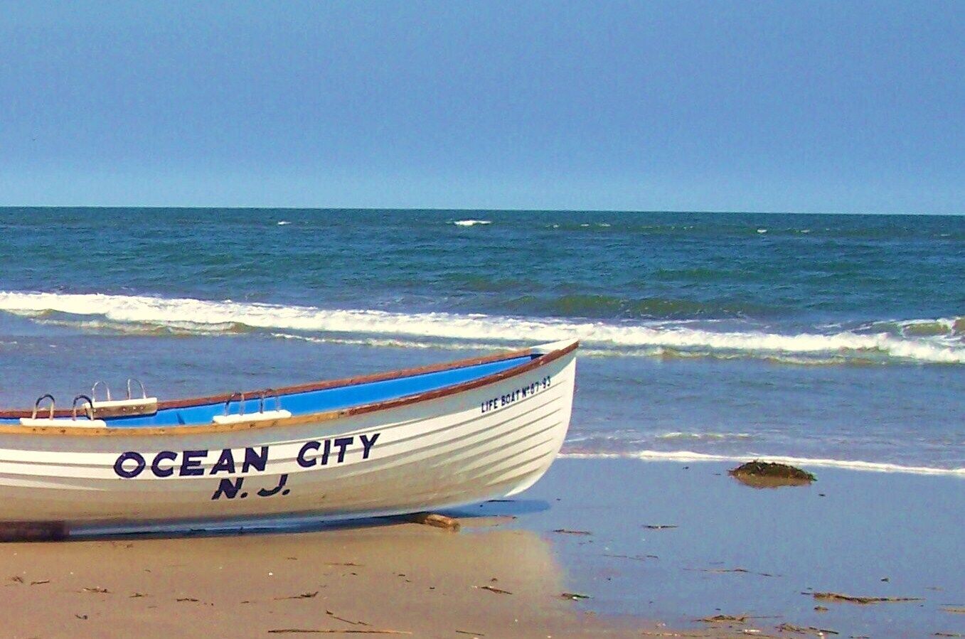 A boat named "Ocean City" on a sandy beach with the ocean in the background.