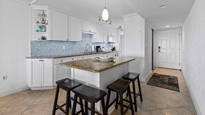 Une cuisine avec des meubles blancs, un pare-feu bleu et un îlot central doté de tabourets.