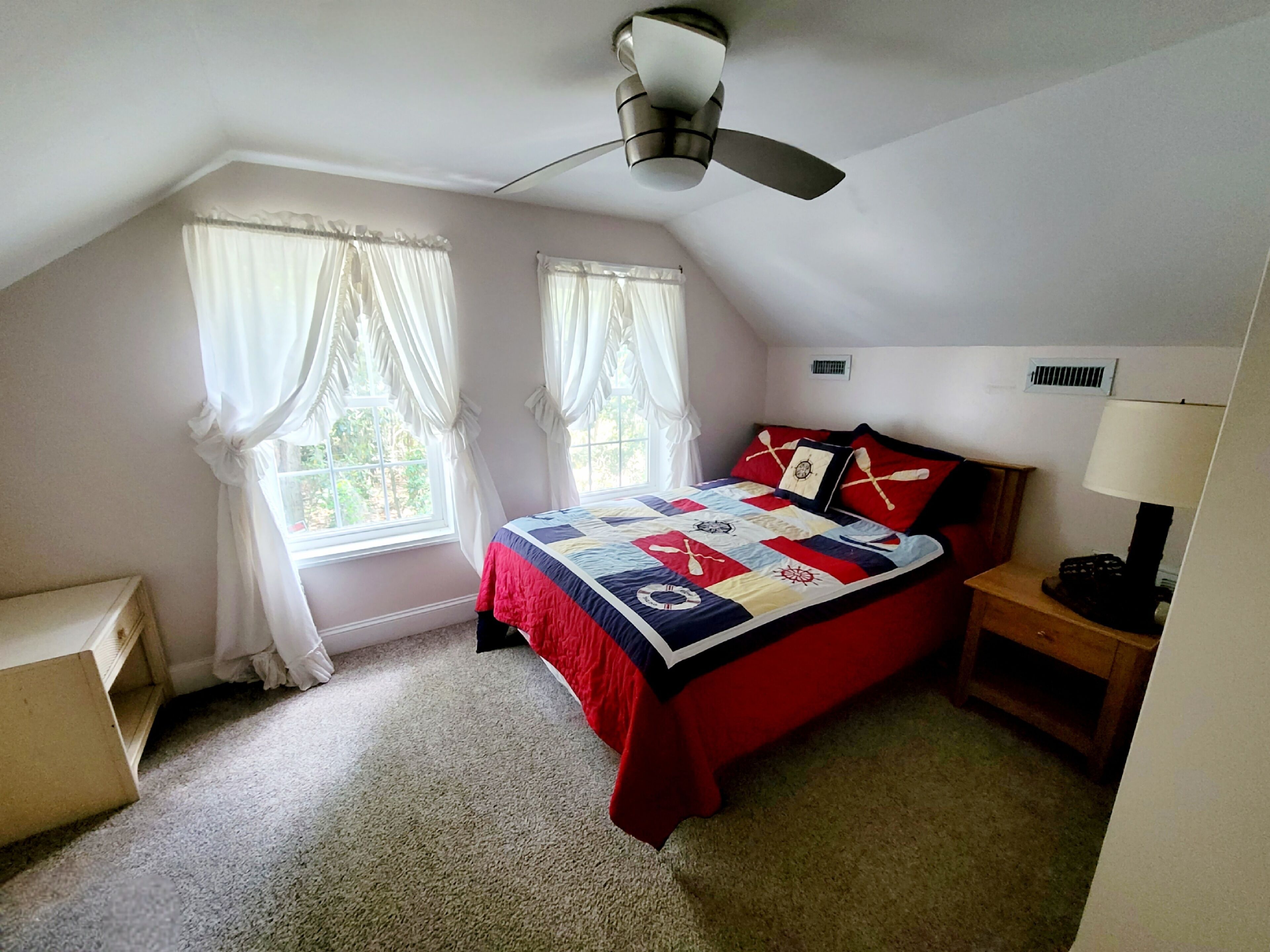Ein Schlafzimmer mit einem Bett, zwei Vorhängen, einem Deckenventilator, einem Nachttisch und einer Lampe.