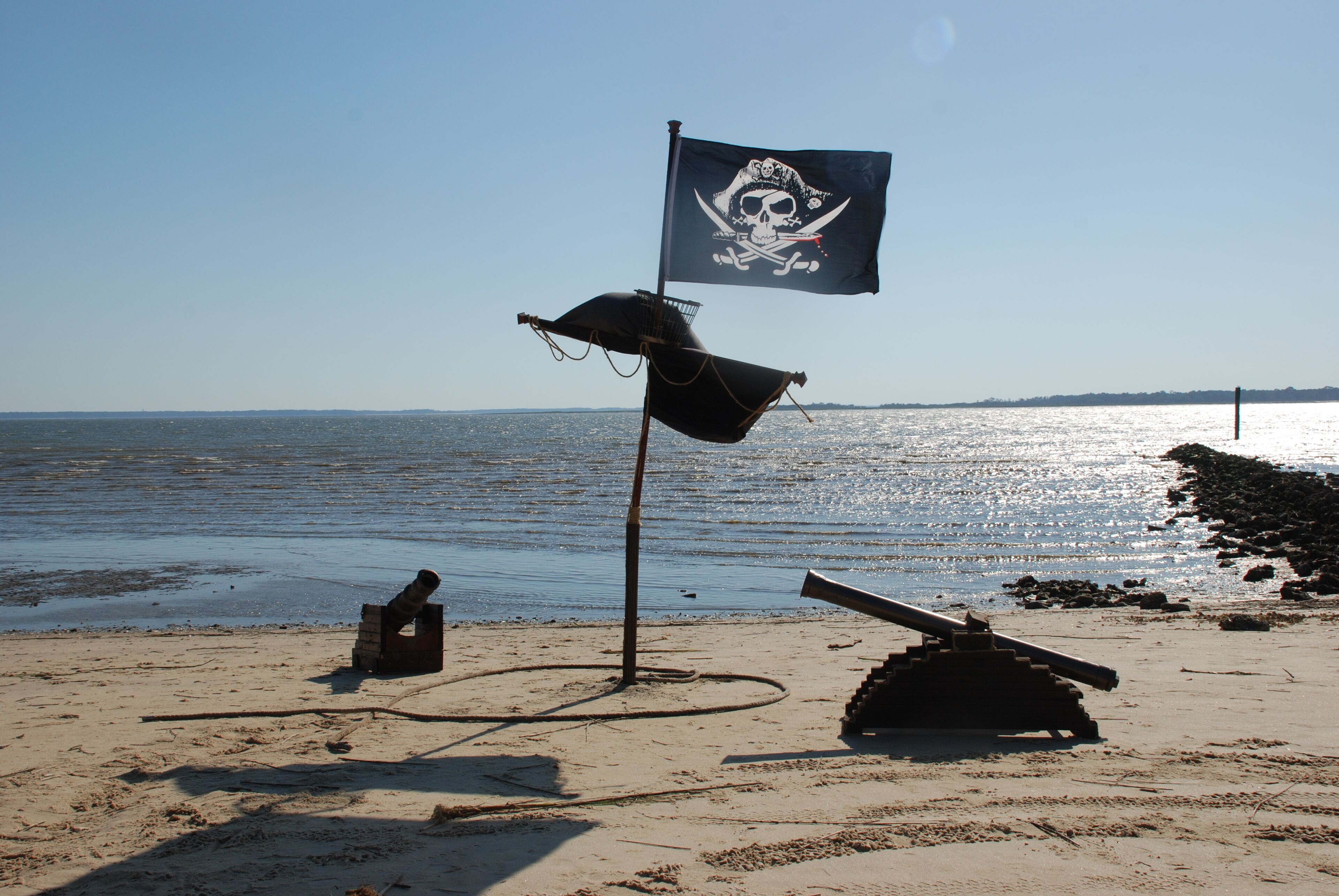 A beach with a pirate flag, a cannon, and a ship's wheel.