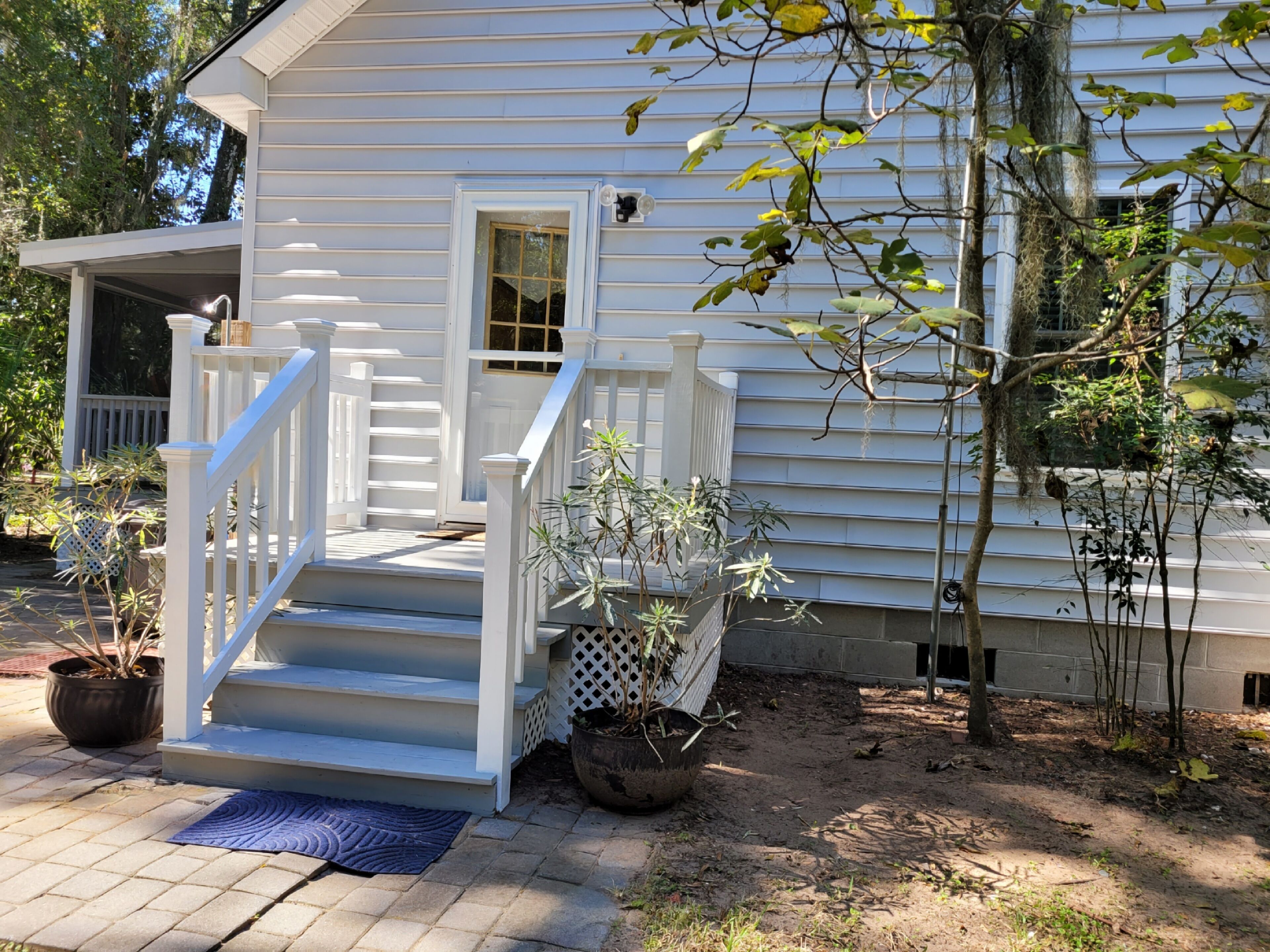 A white house with a front porch, steps, and potted plants.