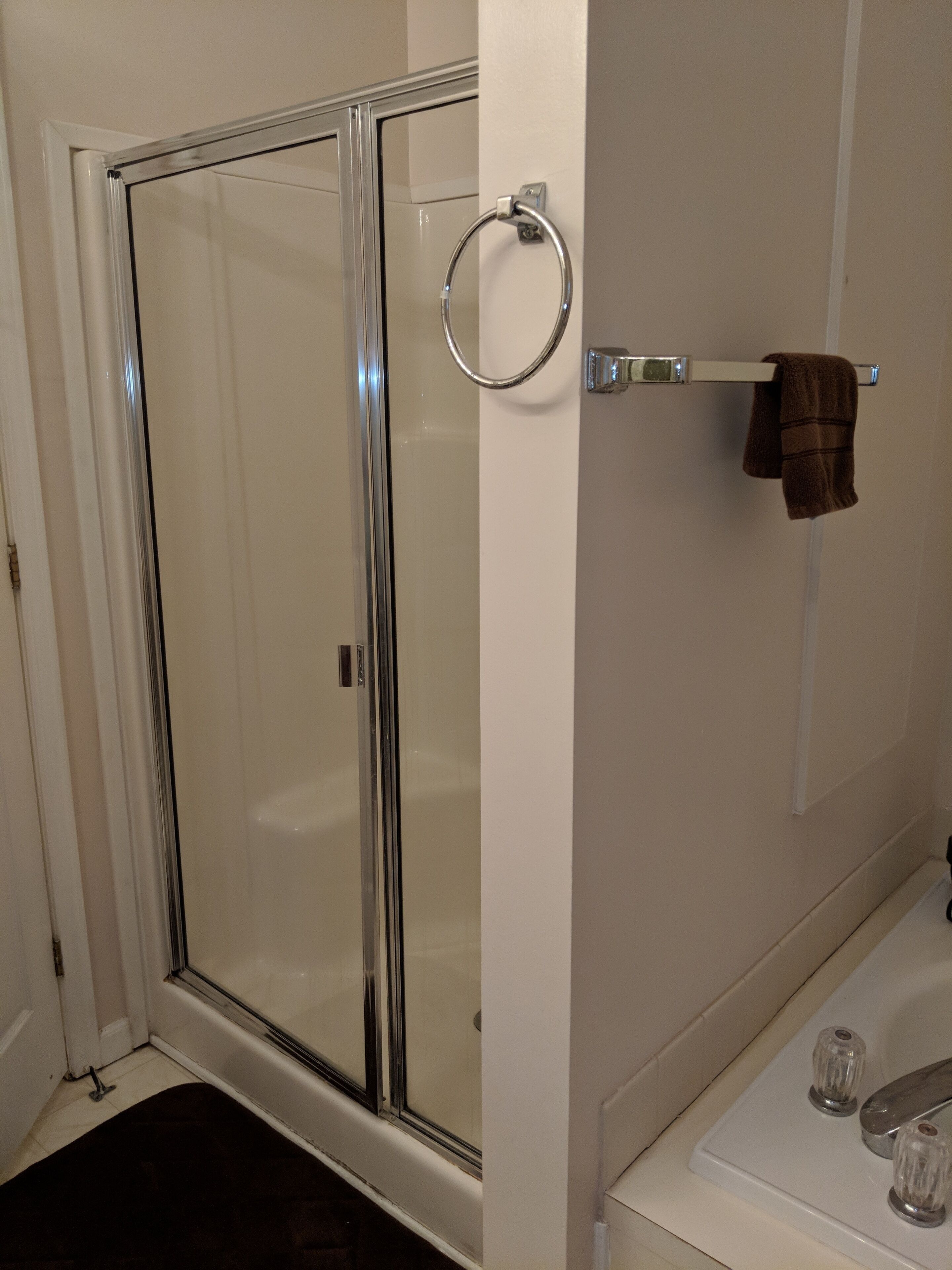 A bathroom with a glass shower enclosure, a towel rack with a towel, and a bathtub with two glass knobs.