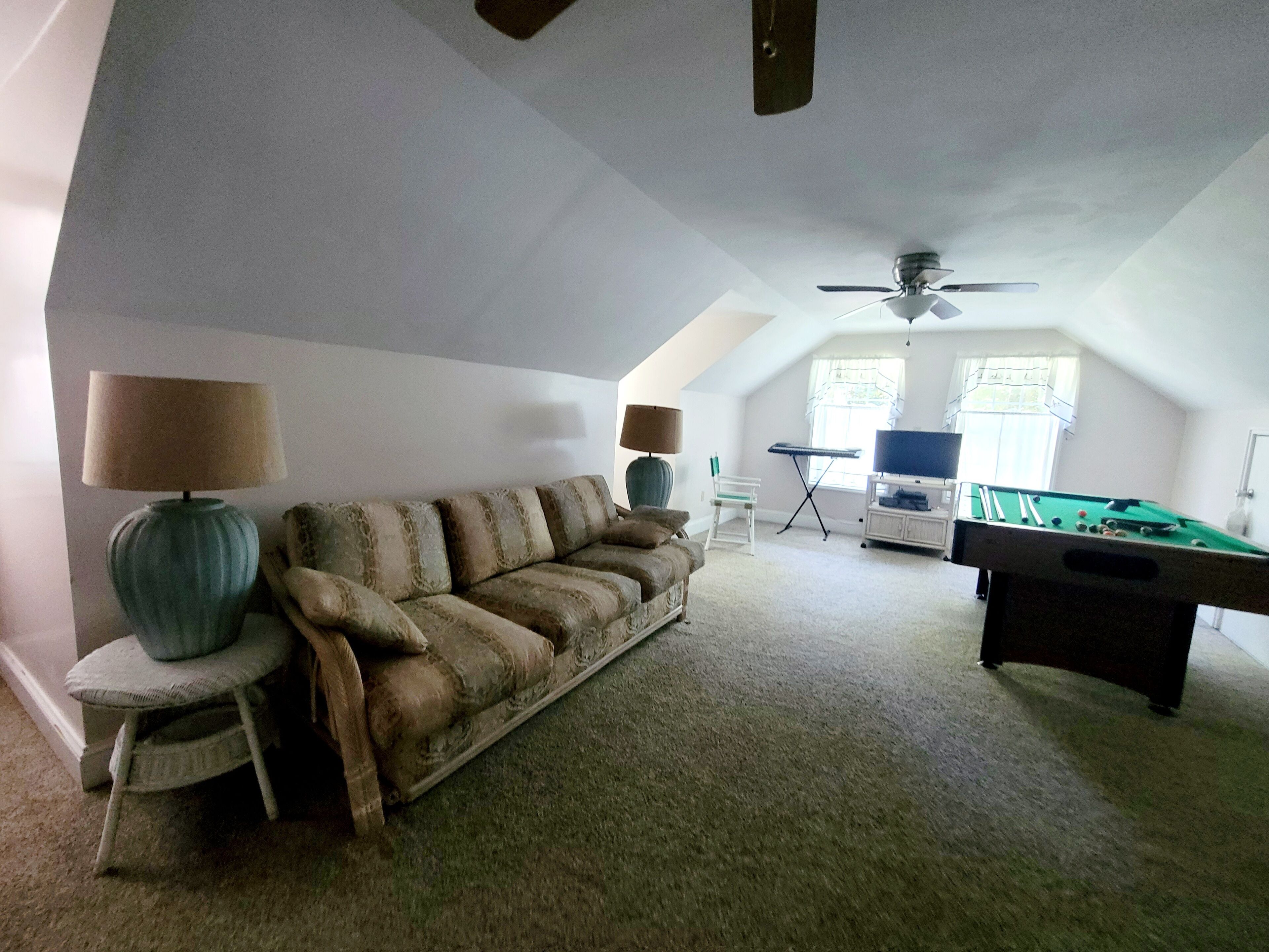 A cozy living room with a sofa, two lamps, a pool table, and a ceiling fan.