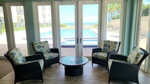 A room with four wicker chairs with floral cushions, a round coffee table, and large glass doors leading to a pool area. - 317 - Fantastic 3 BR Oceanfront Corner (New Smyrna Beach)