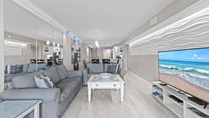 A modern living room with a sofa, coffee table, and a television displaying a beach scene. - 317 - Fantastic 3 BR Oceanfront Corner (New Smyrna Beach)