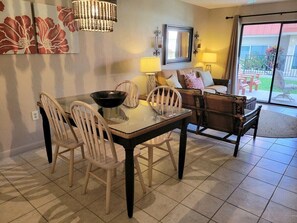 A dining area with a glass table, white chairs, and a dark wooden bench. - 101 - Caribbean décor and a few steps to pool (New Smyrna Beach)
