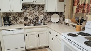 Una cocina con armarios blancos, estufa, lavavajillas y un salpicadero con diseño.