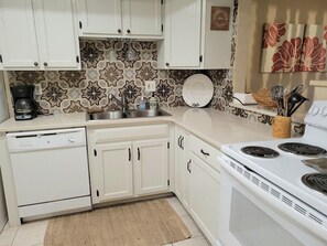A kitchen with white cabinets, a stove, a dishwasher, and a patterned backsplash. - 101 - Caribbean décor and a few steps to pool (New Smyrna Beach)