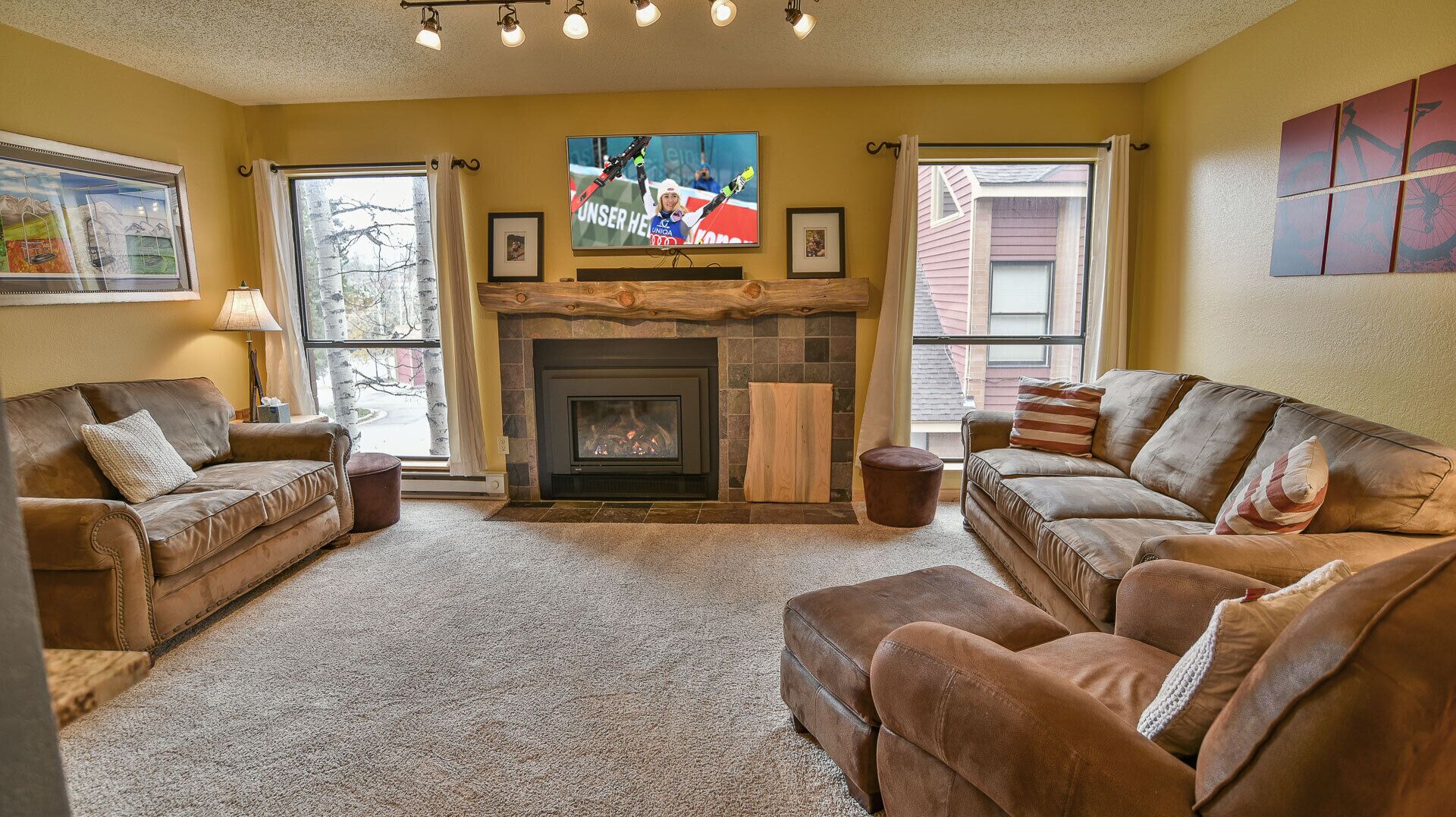 A cozy living room with a fireplace, two sofas, and a television mounted above it.