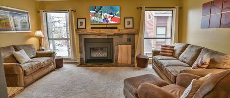 A cozy living room with a fireplace, two sofas, and a television mounted above it.