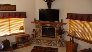 A cozy living room with a stone fireplace, a mounted television, and a bookshelf. - Family Friendly 3 Bedroom, 3 Bath, Mt. Home, Close To 6 World Famous Ski Areas (Dillon)