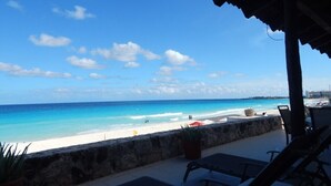 A beach view from a covered patio with lounge chairs and a stone wall.