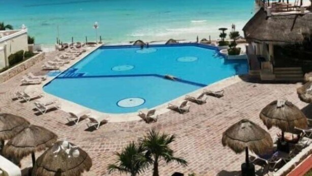A pool area with lounge chairs and umbrellas, a thatched-roof structure, and a view of the ocean.