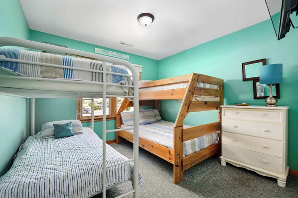 Habitación con literas de madera y una cama individual, un aparador y una ventana.