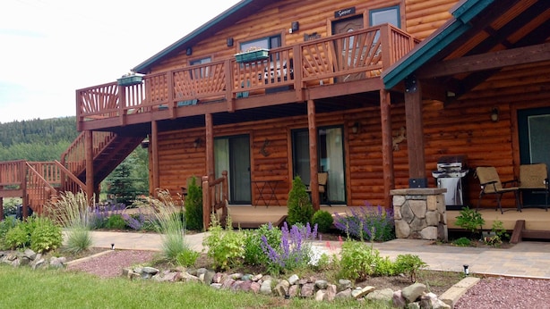 A wooden cabin with a balcony, a stone fireplace, and a patio area with outdoor seating. - All-Season Vacation Getaway with Stunning Views! (East Glacier Park)
