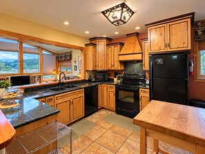 A kitchen with wooden cabinets, a black refrigerator, a stove, and a microwave. - All-Season Vacation Getaway with Stunning Views! (East Glacier Park)