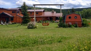 A log cabin with a porch, a swing, and a garden with flowers and a swing set. - All-Season Vacation Getaway with Stunning Views! (East Glacier Park)