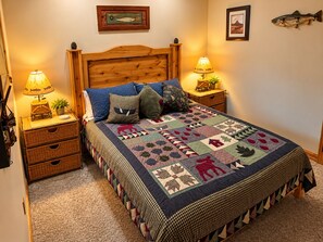 A bedroom with a wooden headboard, a quilted bedspread, two bedside tables with lamps, and a wall-mounted fish decoration. - All-Season Vacation Getaway with Stunning Views! (East Glacier Park)