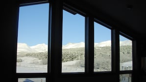 A room with large windows offering a view of snow-covered mountains and a clear blue sky. - All-Season Vacation Getaway with Stunning Views! (East Glacier Park)