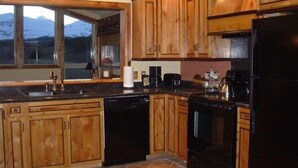A kitchen with wooden cabinets, a black refrigerator, and a window with a mountain view. - All-Season Vacation Getaway with Stunning Views! (East Glacier Park)