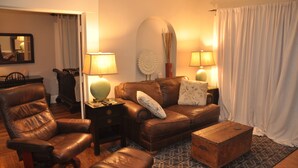 Ein Wohnzimmer mit Ledersessel, Sofa, Couchtisch aus Holz und zwei Lampen.