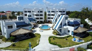 Un resort moderno con varias construcciones blancas, una piscina central y estructuras con techo de paja.