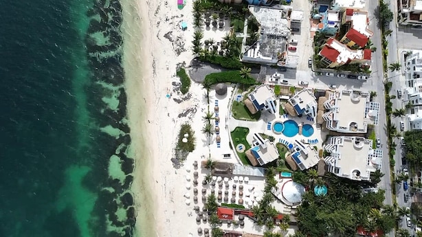 Vista aérea de un complejo turístico costero con múltiples piscinas, acceso a la playa y diversas edificaciones.