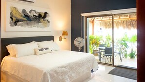 Un dormitorio con cama, ventilador de techo, aire acondicionado, lámpara de pared y puerta corrediza de vidrio que da a un espacio exterior con mesa y sillas.